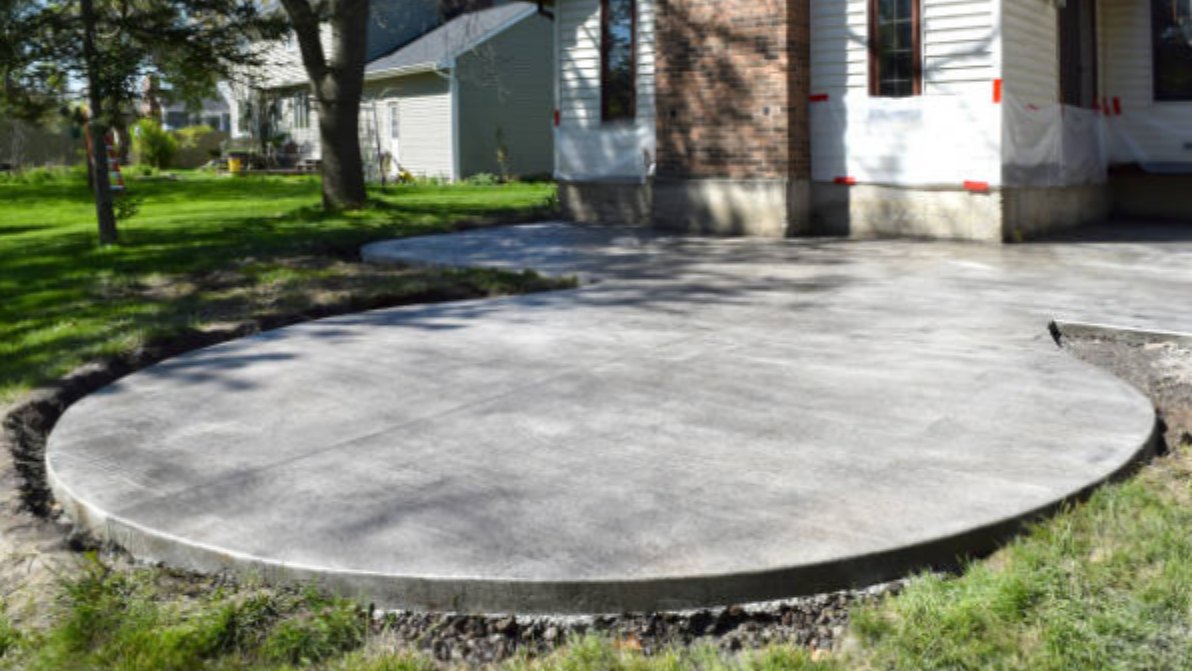 Curved concrete patio with saw-cut joints poured against an older brick home