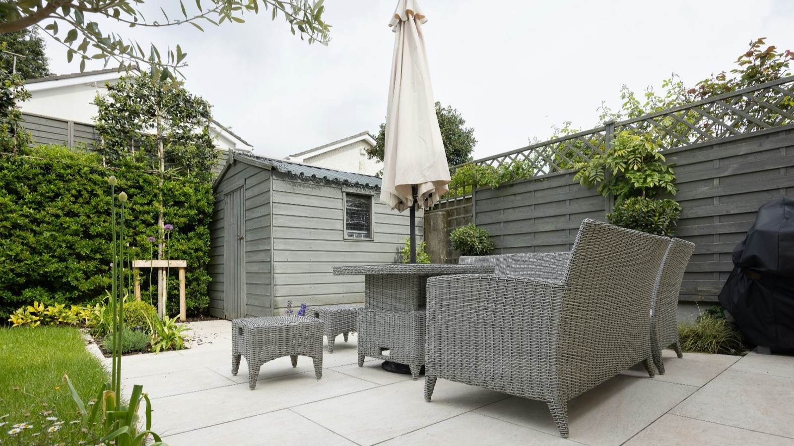 Large-format concrete patio with outdoor furniture and an umbrella in an enclosed back garden