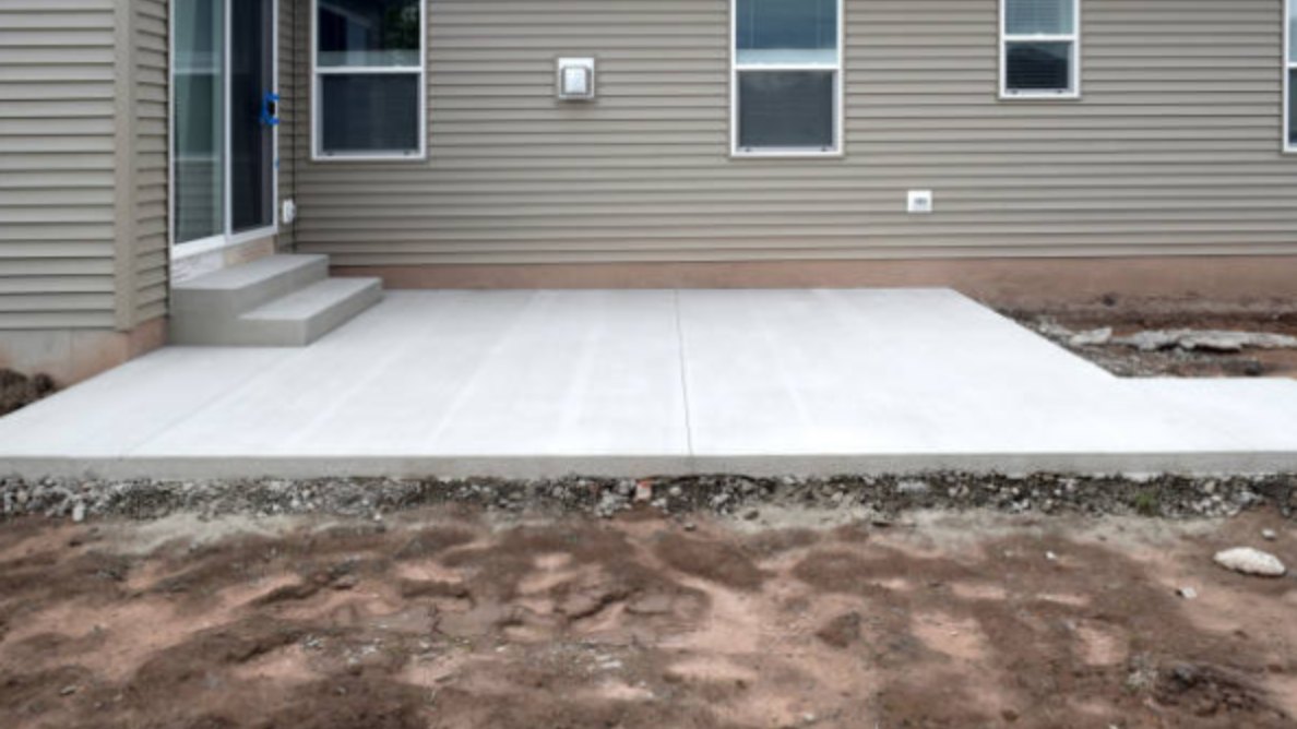New backyard concrete patio slab and poured steps, with bare graded soil still around the edges