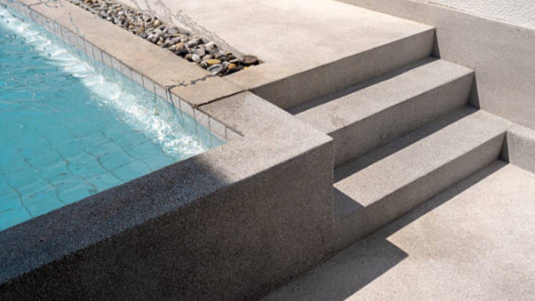 Exposed aggregate concrete steps and deck edge beside a pool