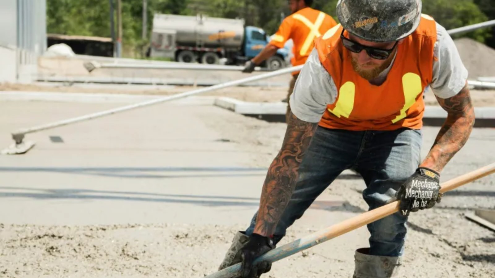Concrete worker in a hard hat raking fresh mix out to grade between the forms